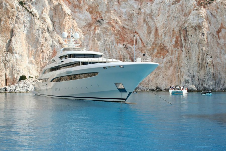 A white superyacht anchored in calm blue water beneath towering limestone cliffs