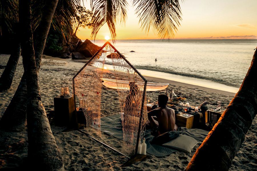 A couple at a candlelit private dinner on the beach at sunset